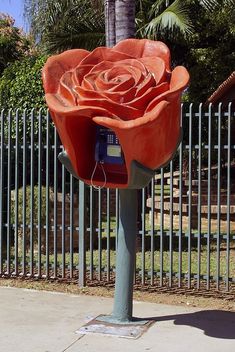 an orange flower shaped phone booth sitting on the side of a road next to a fence