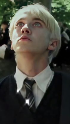 a man with blonde hair wearing a black vest and tie looking up at the sky