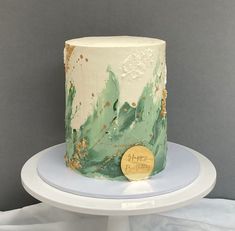 a white and green cake with gold leaf decorations on it's side sitting on a plate