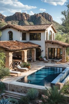 an outdoor swimming pool in front of a large house with mountains in the back ground