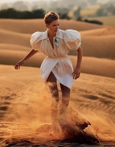 a woman standing on top of a sand dune in the middle of the desert wearing a white dress