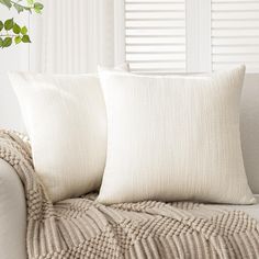 two white pillows sitting on top of a couch next to a plant in a vase