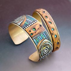 two bracelets with designs on them sitting on a table