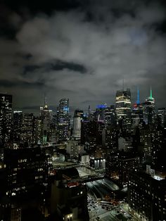 the city skyline is lit up at night with bright lights and clouds in the sky