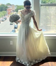 a woman in a white dress standing by a window