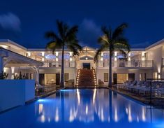 an outdoor swimming pool with lounge chairs and palm trees in the background at night time