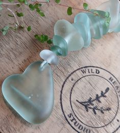 two sea glass hearts sitting on top of a wooden table next to a green plant