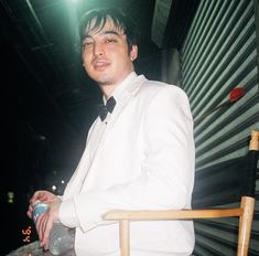 a man in a white suit and black tie sitting on a chair