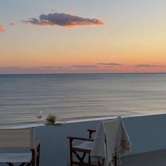 two wooden chairs sitting on top of a balcony next to the ocean at sunset or dawn