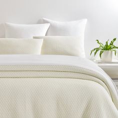 a bed with white sheets and pillows on top of it next to a potted plant