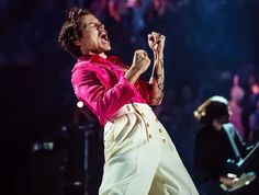 a male in a pink shirt and white pants on stage with his hands up to his mouth