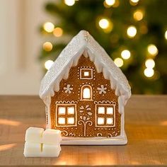 a lit gingerbread house next to a christmas tree