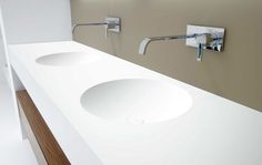 two white sinks in a bathroom with wood trim around the sink and faucets on the wall