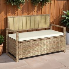 a wicker bench sitting next to a wooden wall with potted plants on it