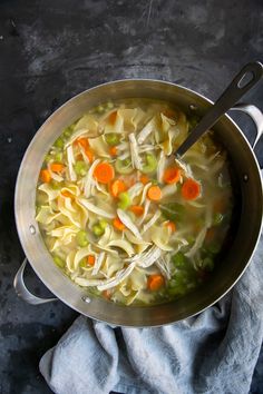 a pot filled with chicken noodle soup on top of a blue towel next to a spoon