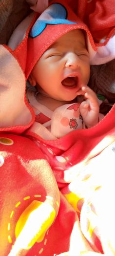 a baby is laying down with its mouth open and wearing a red hat on top of it's head