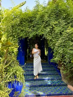 a woman in a white dress is walking up some stairs with blue tiles on the ground