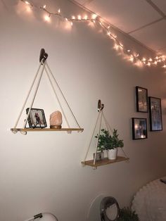 two hanging shelves with plants and pictures on them in a room decorated with string lights