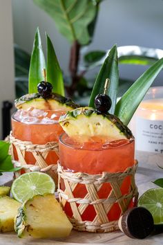 two glasses filled with drinks sitting on top of a table next to sliced pineapples