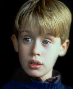 a young boy with blond hair and blue eyes looks at the camera while wearing a sweater