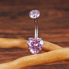 a pink heart shaped jeweled ring sitting on top of a piece of wood