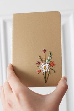 a hand holding a brown notebook with flowers on it