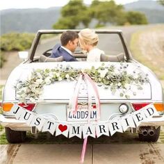 a bride and groom are sitting in the back of a convertible car with just married banner