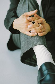 a person sitting on the ground with their hands folded over their legs and wearing a ring