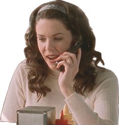 a woman sitting at a table talking on her cell phone while holding a juice box