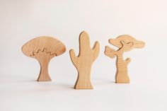 three wooden toy animals standing next to each other on a white surface and one is holding a cactus