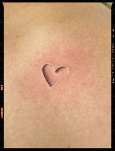 a woman's back with a small heart tattoo on the side of her chest