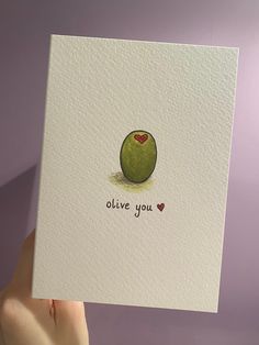 a hand holding up a card with an olive on it that says, i love you