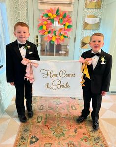 two young boys in tuxedos holding a sign