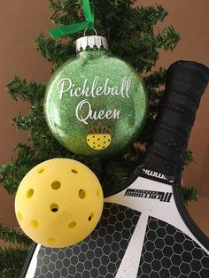 a pickleball christmas ornament next to a tennis racket and ball