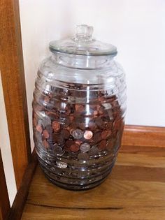 a glass jar filled with coins sitting on top of a wooden floor next to a wall