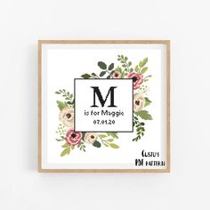 a cross stitch pattern with the letter m and flowers on it, in a wooden frame