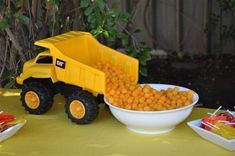 a yellow toy dump truck sitting next to a bowl of food on top of a table