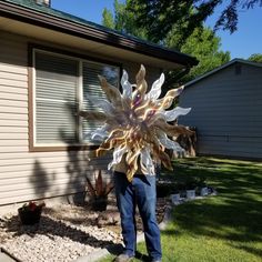 a man standing in front of a house holding a large metal sunflower decoration on his head