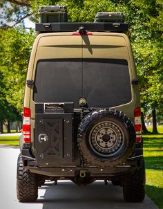 the back end of a vehicle parked in front of a tree lined park area with green grass and trees