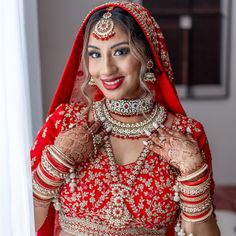 a woman in a red and gold bridal outfit posing for the camera with her hands on her chest