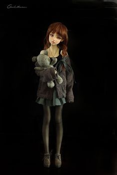 a doll is holding a teddy bear in her arms while standing on a black background