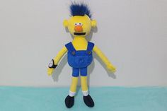 a yellow stuffed toy with blue overalls and a mohawk on it's head