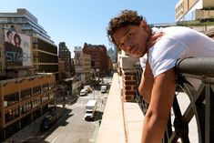 a man leaning on the side of a building with his hand on his head and looking at the camera