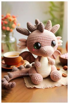 a crocheted dragon sitting on top of a wooden table next to a cup of coffee