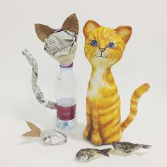 two cats made out of paper sitting next to each other with fish on the ground