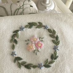 a close up of a pillow on a bed with flowers and leaves embroidered on it