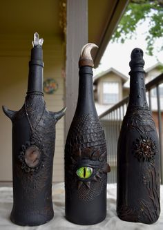 three black bottles with green eyes and horns on them sitting on a table in front of a house