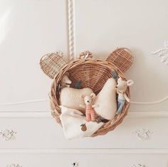 two stuffed animals in a basket hanging on the wall above a dresser with white drawers