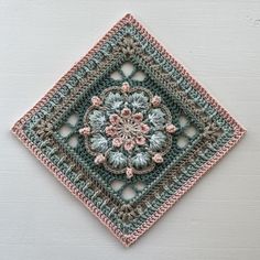 a crocheted square with a flower in the center on a white wall background