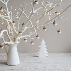 a white vase filled with christmas ornaments next to a small tree covered in mini lights